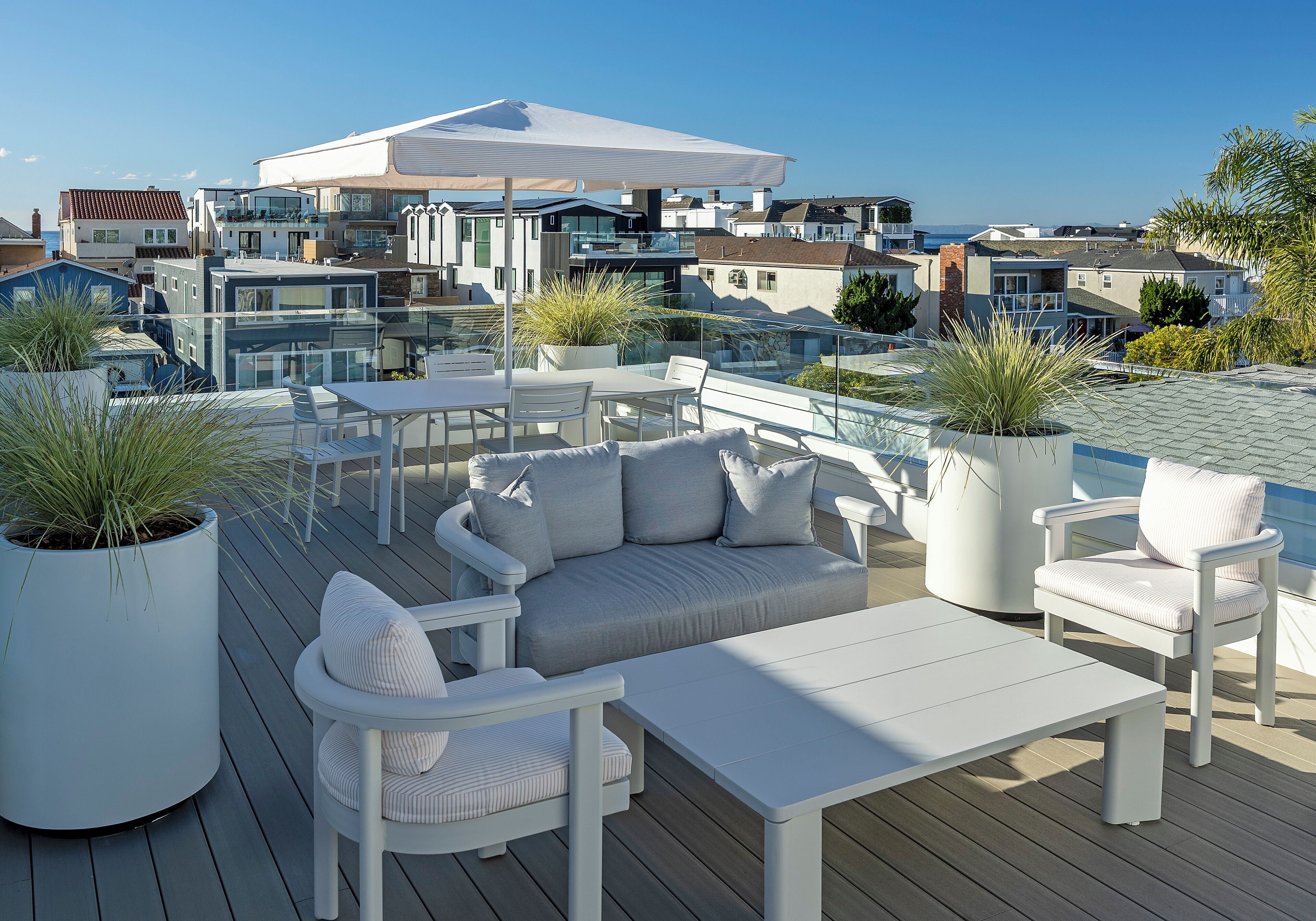 A modern outdoor deck with white furniture, potted plants, and a view of coastal buildings.