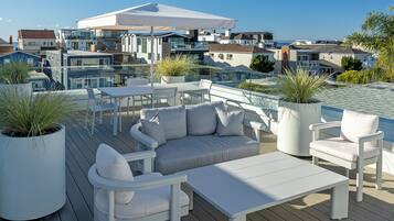 A modern outdoor deck with white furniture, potted plants, and a view of coastal buildings.