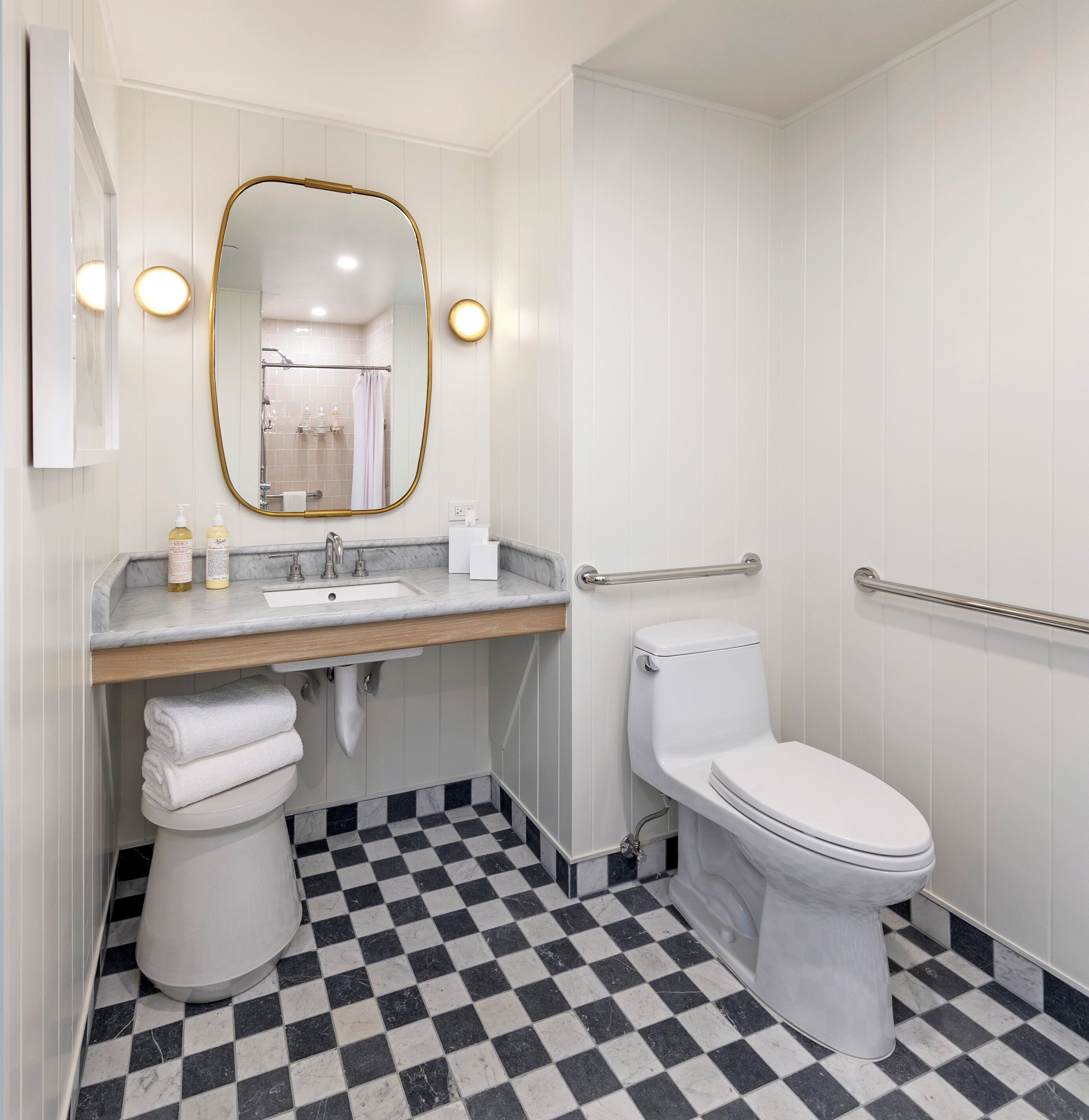 A bathroom with a white toilet, a sink with a marble countertop, a mirror with a gold frame, and a checkered floor.