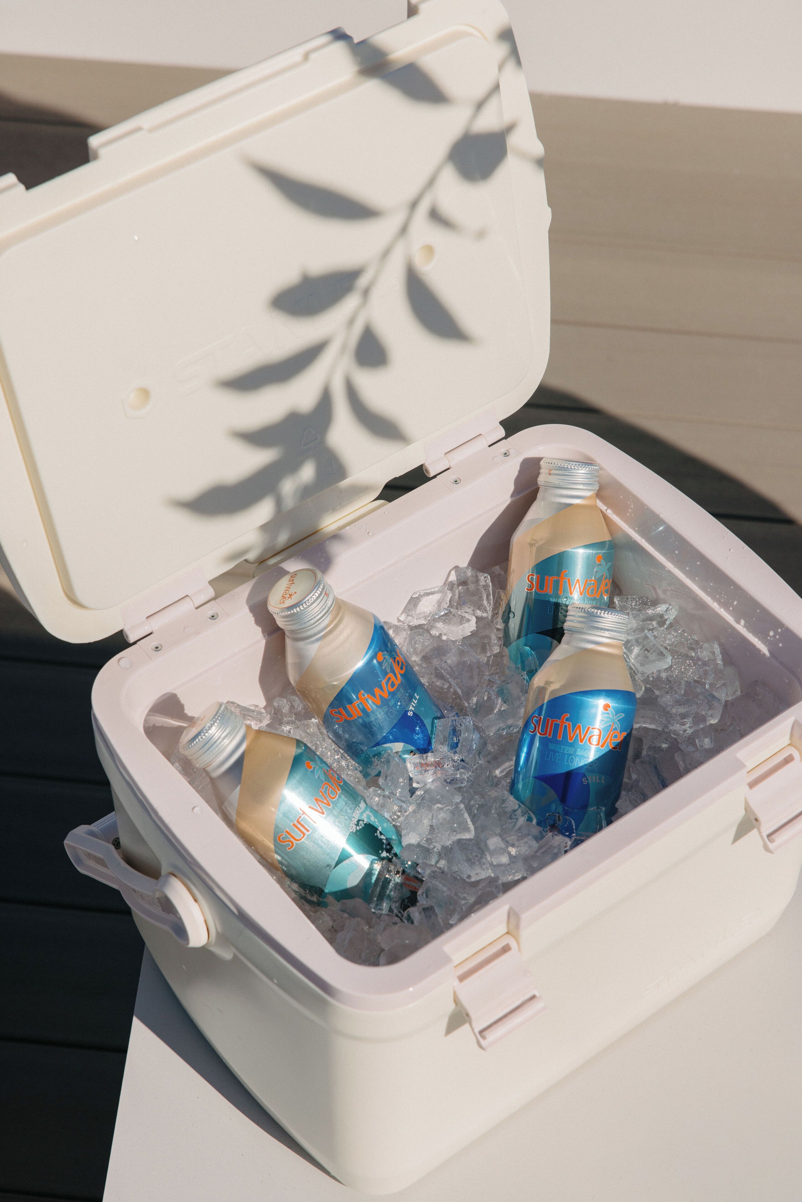 A portable cooler with a lid open, containing several bottles of Surfwater.