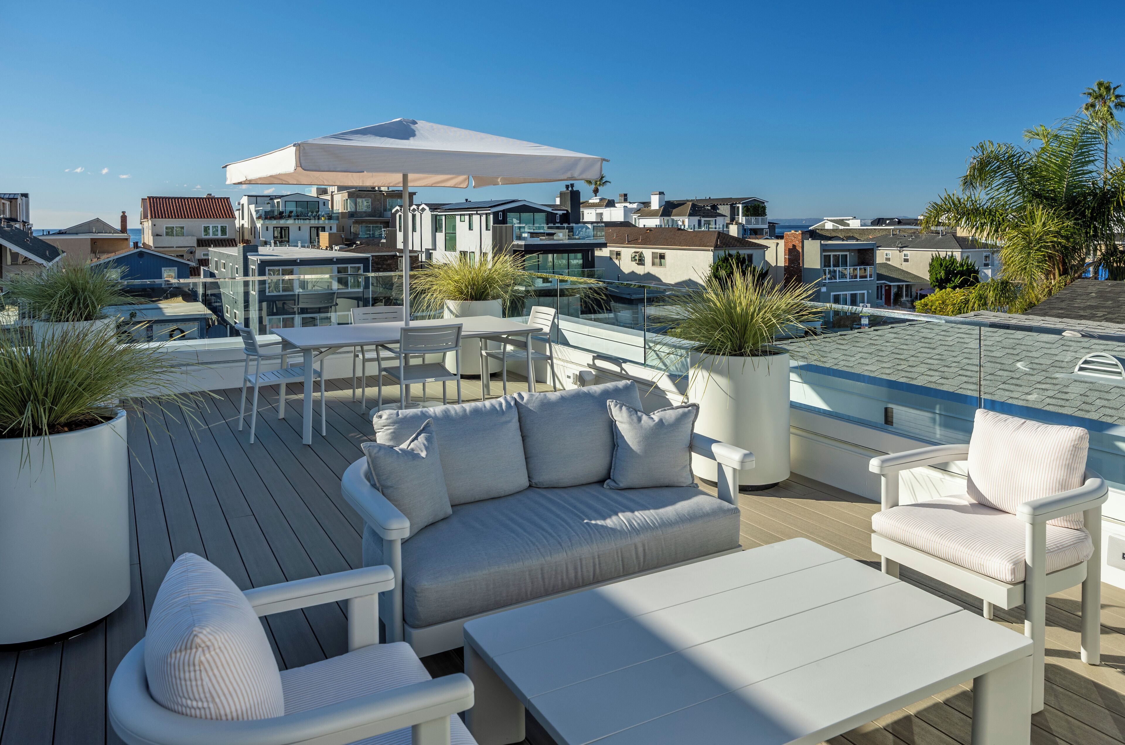 Terraza en la azotea con sofá, sillas y una mesa, rodeada de plantas en macetas y vistas a una zona residencial.