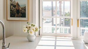 A kitchen with a large window, a pendant light, a sink, and a framed picture on the wall.