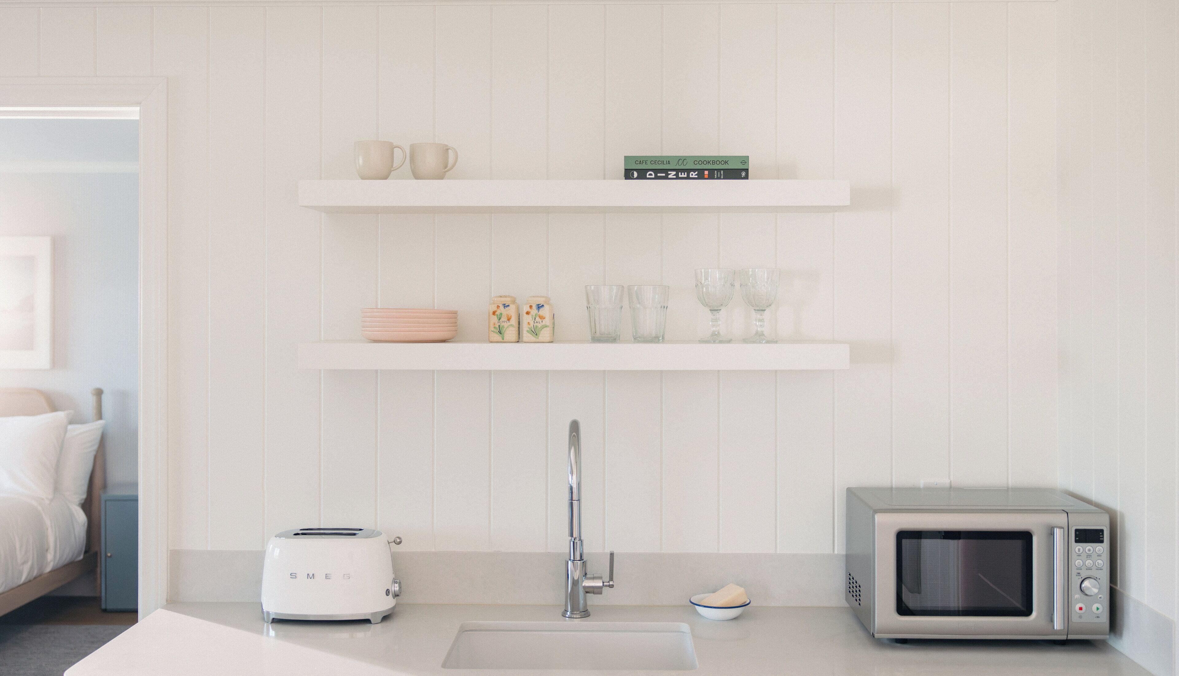 A kitchen with a toaster, a microwave, a sink, and shelves with kitchenware.