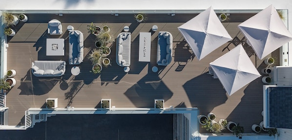 Vista aérea de una terraza en la azotea con asientos al aire libre, sombrillas y plantas en macetas.