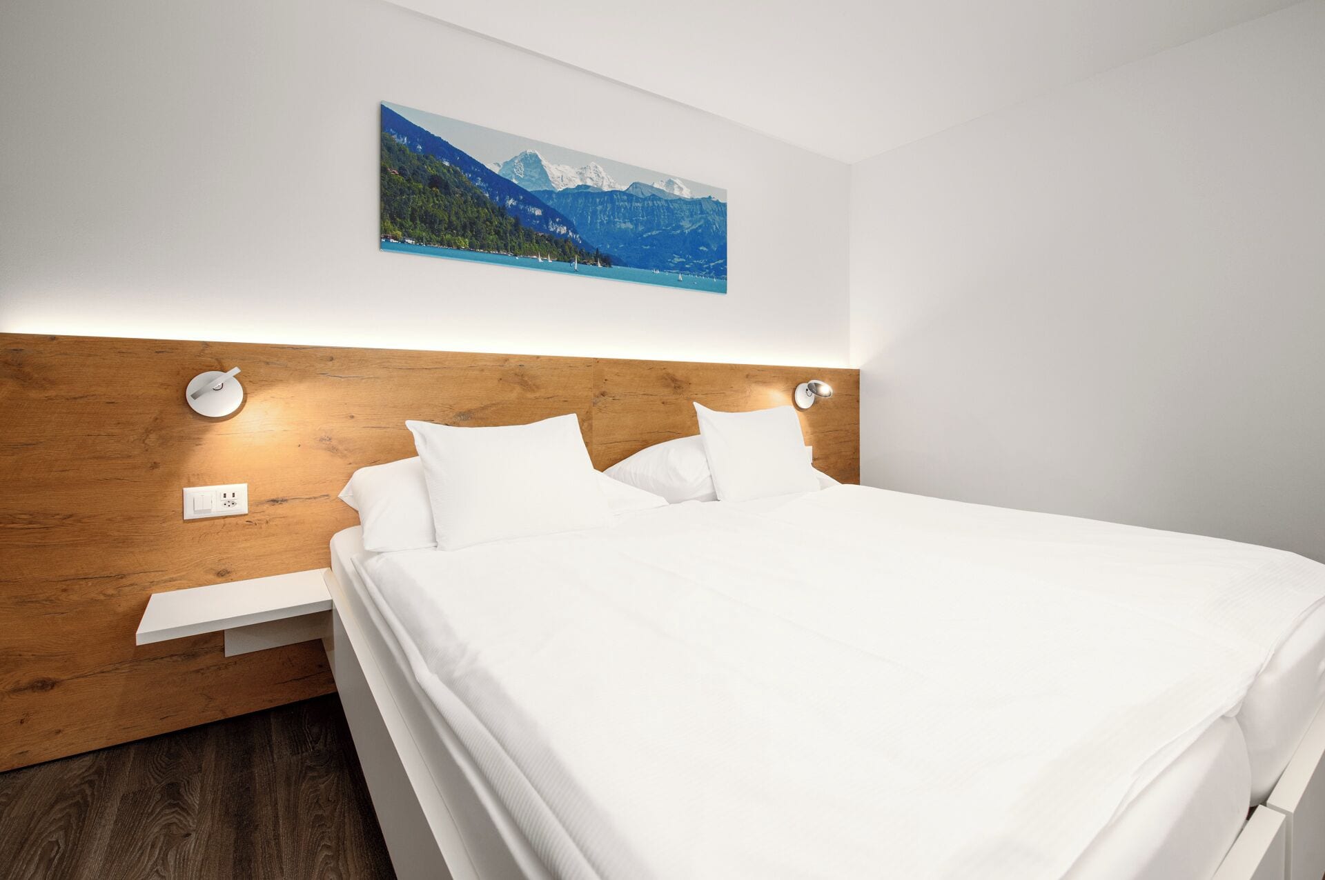 Cama bem arrumada com lençóis brancos, cabeceira de madeira e uma pintura de paisagem montanhosa acima.