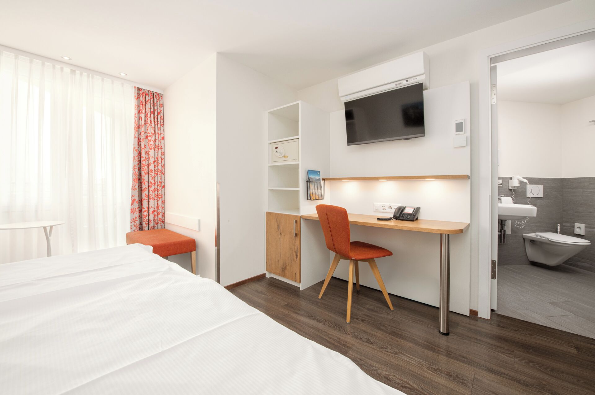 Une chambre d’hôtel comprenant un lit, un bureau avec une chaise, une télévision, une petite étagère et une salle de bain.