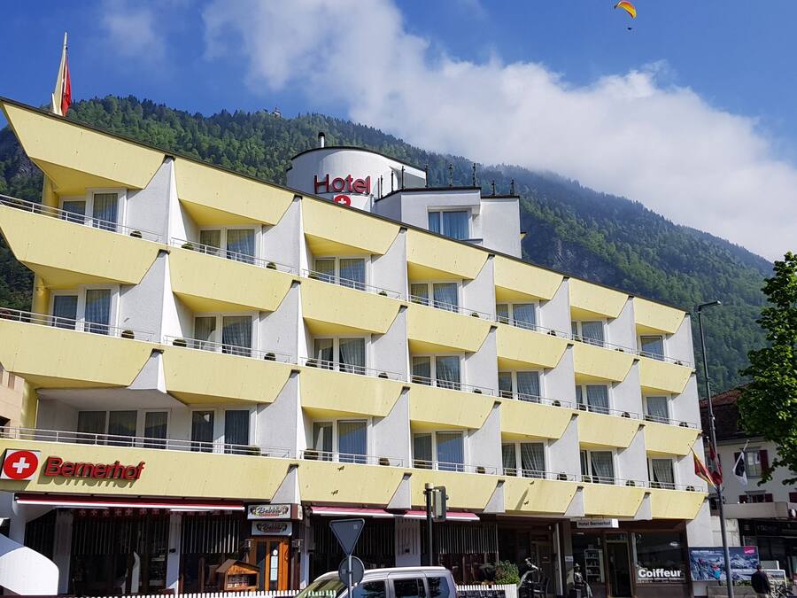 Un hôtel à plusieurs étages, avec une façade jaune, des balcons et une vue sur les montagnes en arrière-plan.