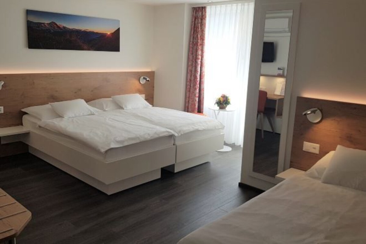A modern hotel room with a large bed, a small bedside table, a nightstand, a mirror, and a painting on the wall.