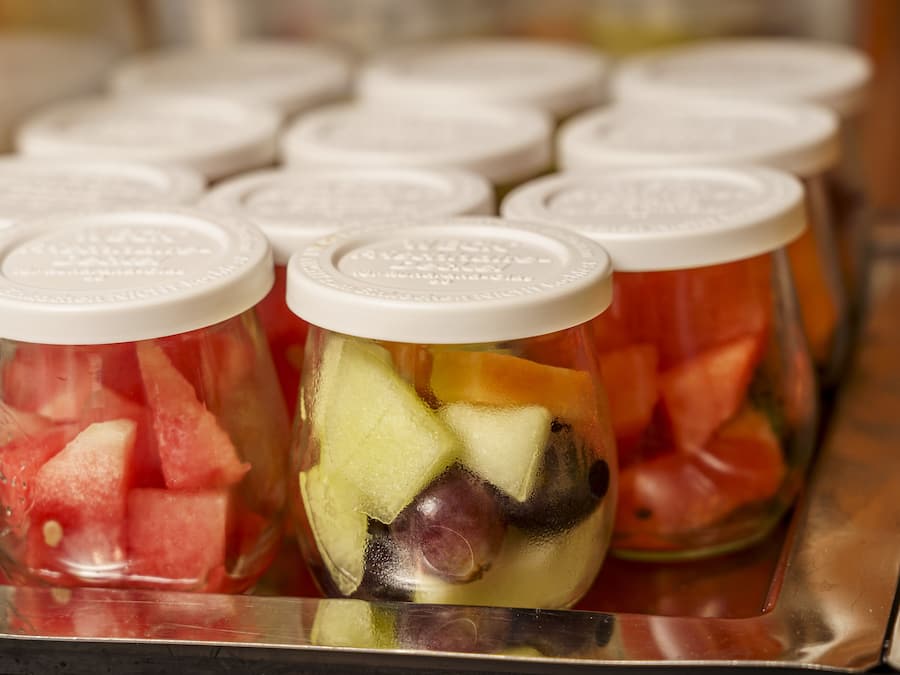 Several glass jars with white lids, filled with various fruits like watermelon and melon.