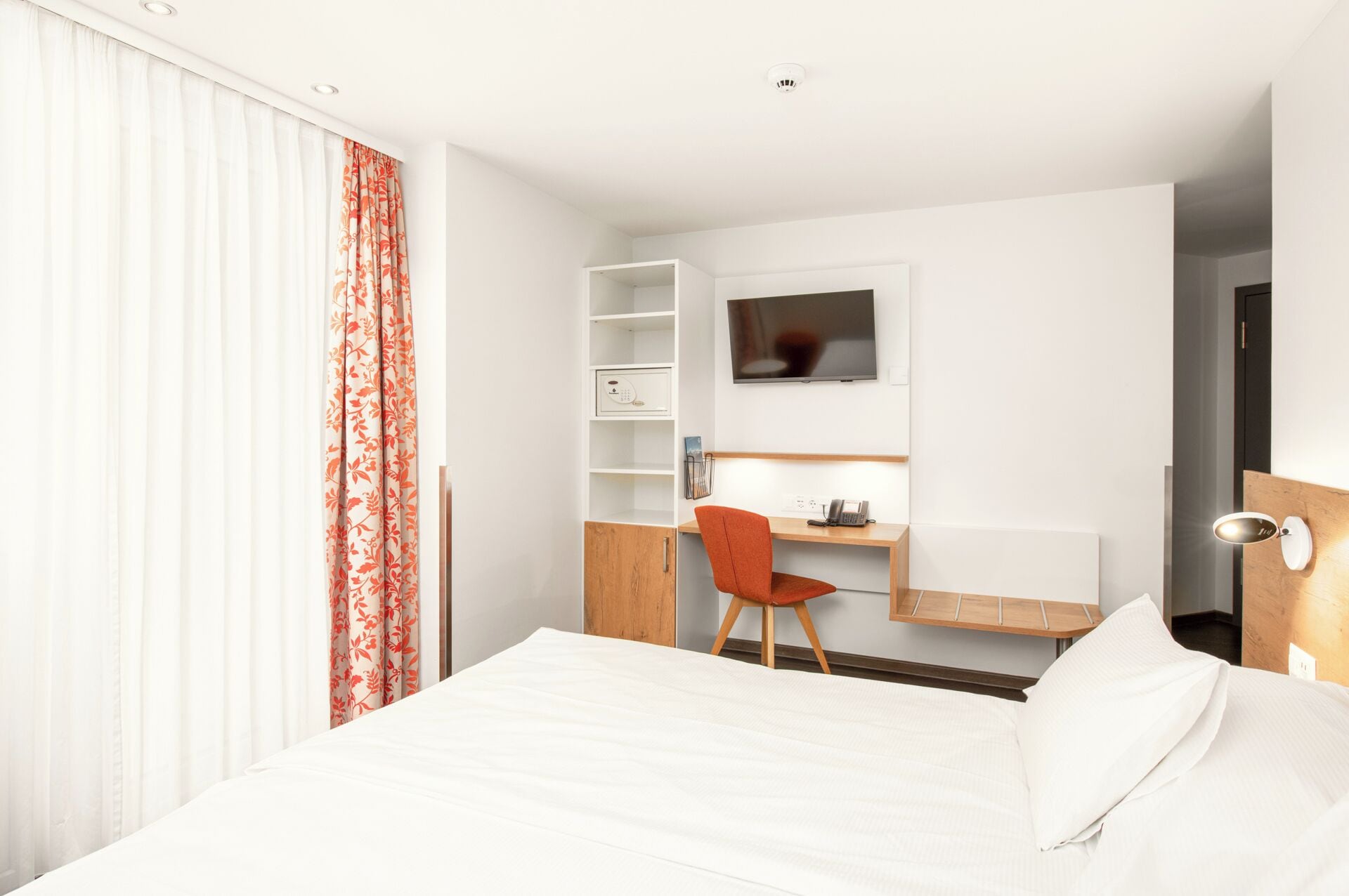 A hotel room with a bed, a desk with a chair, a TV, and a phone.