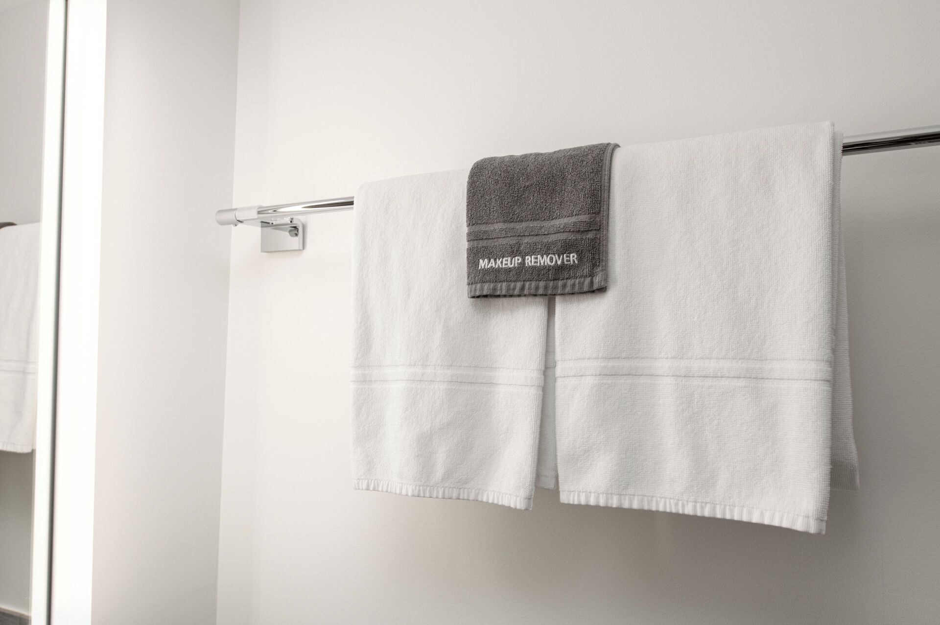 A bathroom with two white towels hanging on a metal towel rack, one of which has a label reading 'MAKEUP REMOVER.'