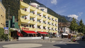 Un hotel con fachada amarilla, balcones con jardineras florales y un toldo rojo.
