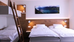 Un dormitorio con literas, cabecero de madera, mesita de noche, lámpara de pared y un cuadro de un paisaje enmarcado.
