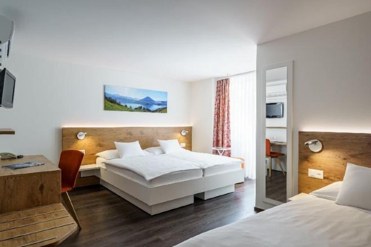 Una habitación de hotel con cama, escritorio, silla y un cuadro en la pared.