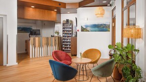 Un interior moderno con suelo de madera, un mostrador de recepción, una estantería y una zona de comedor con sillas.
