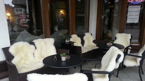 Un área de estar al aire libre con sillas y mesas de mimbre, algunas con mantas de piel blanca.