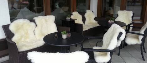 Un área de estar al aire libre con sillas y mesas de mimbre, algunas con mantas de piel blanca.