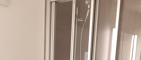 A modern bathroom with a glass-enclosed shower, a toilet, and a wall-mounted faucet.