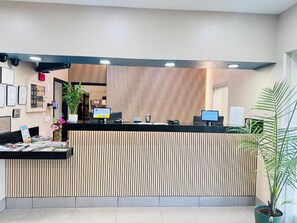 A reception desk with a modern design, featuring a vertical wooden panel backdrop, a black counter, and a potted plant to the right. - Country Inn & Suites by Radisson, Bismarck-Mandan (Bismarck)