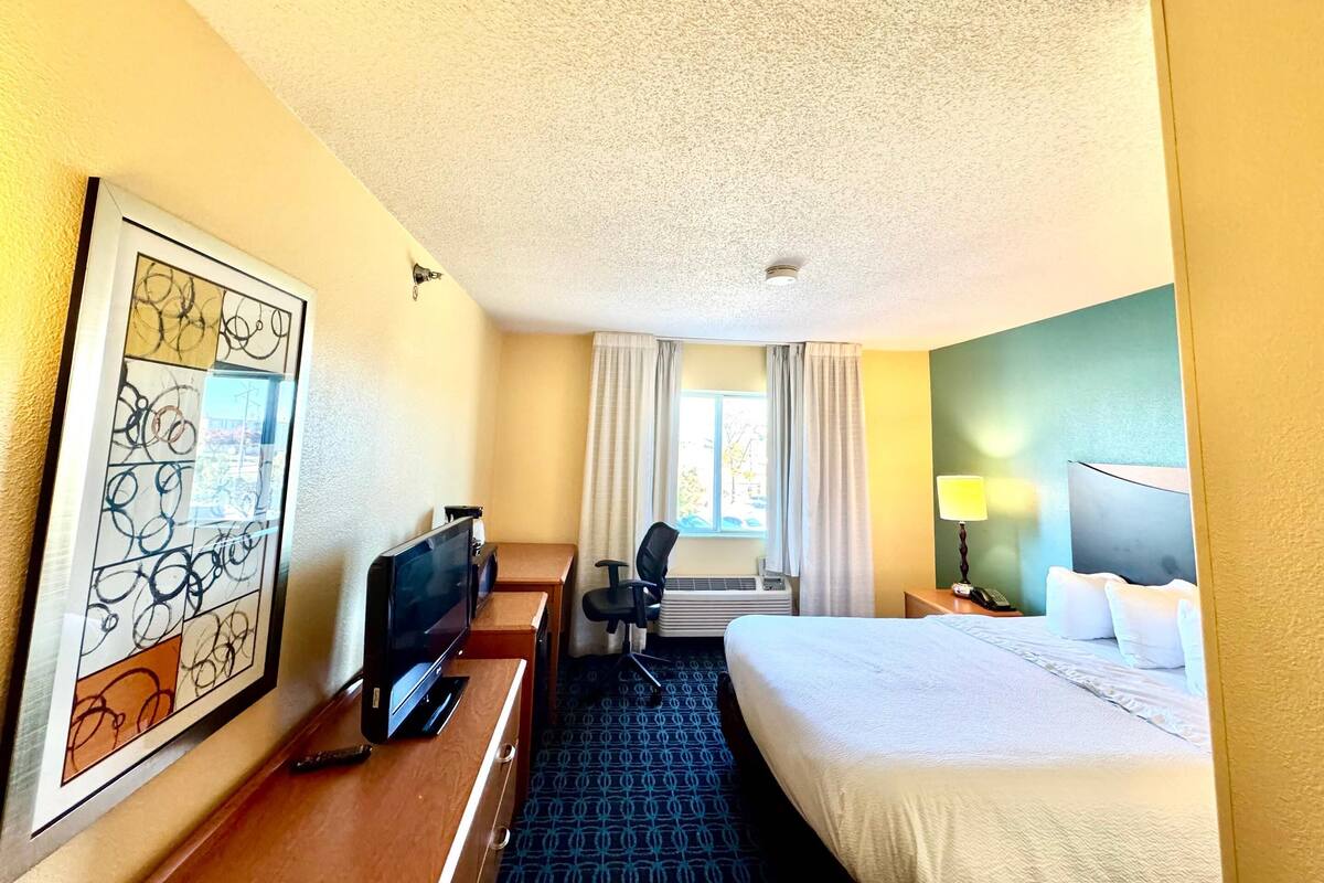 A hotel room with a bed, a desk with a TV, a chair, a lamp, and a window with curtains.