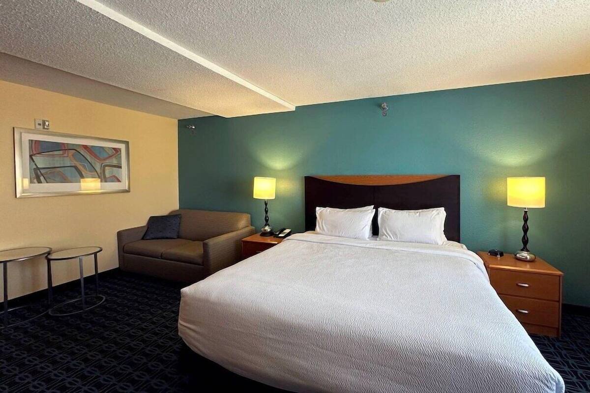 A hotel room with a large bed, two bedside tables with lamps, a sofa, a small table, and a painting on the wall.