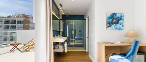 Una habitación moderna con un escritorio de madera, una silla azul, ducha de vidrio y vistas a la ciudad.