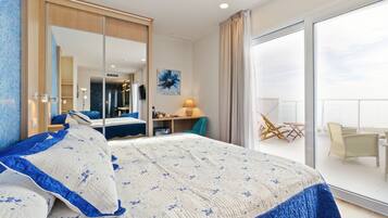 A modern hotel room with a large bed, a sliding glass door to a balcony, a desk, and a chair.