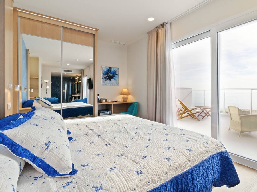 Una habitación de hotel moderna con una cama grande, un ventanal corredero a un balcón, un escritorio y una silla.
