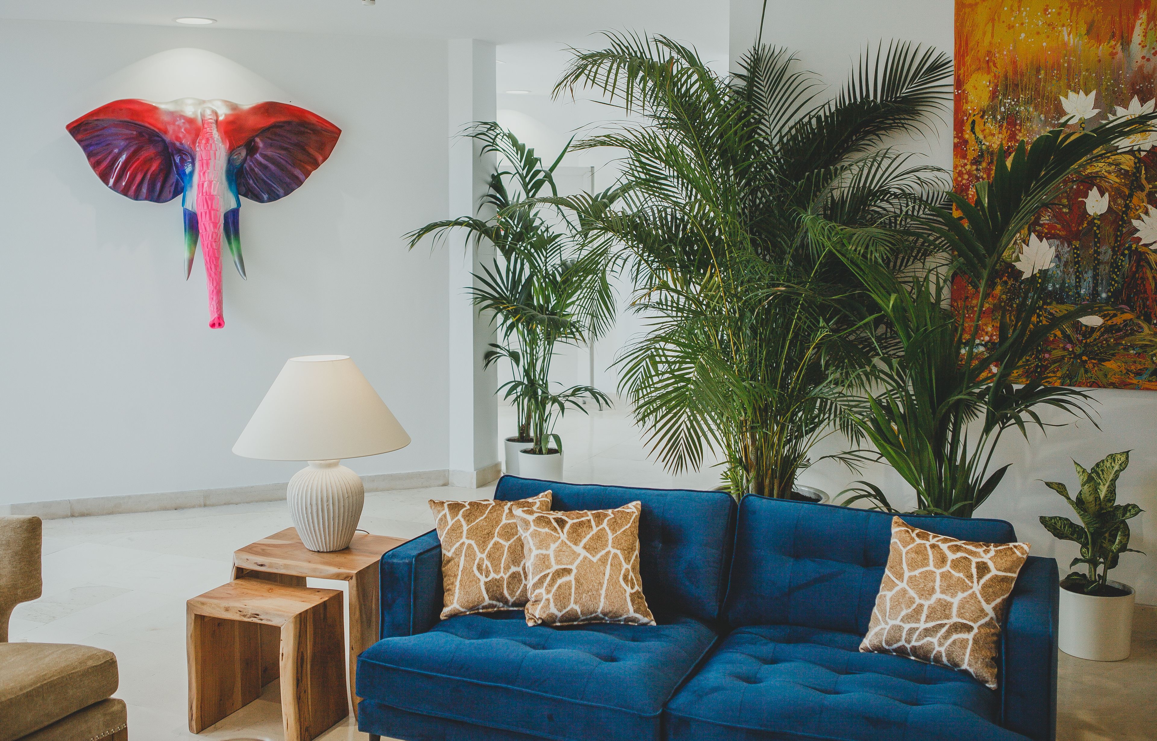 Ein modernes Wohnzimmer mit einem blauen Sofa, zwei Holznachttischen, einer weißen Lampe und einer großen Kübelpflanze.
