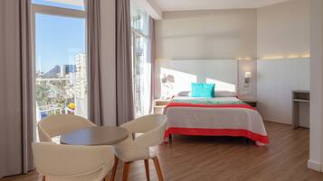 Habitación de hotel con cama, una mesa, dos sillas, una mesita de noche y vistas a la ciudad.