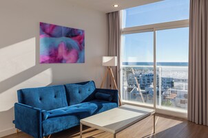 A modern living room with a blue sofa, a white coffee table, and a large window offering a city view.