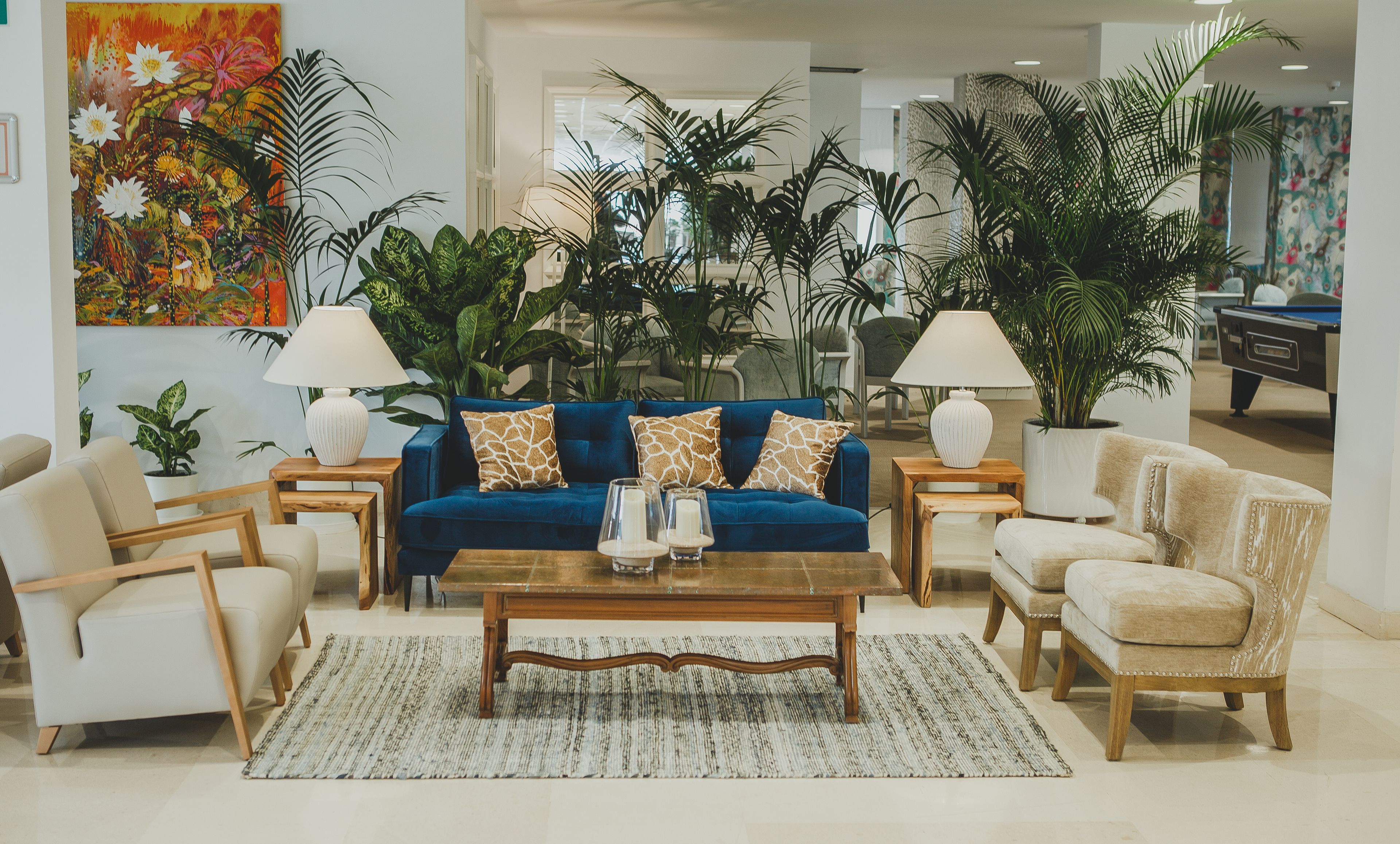 A living room with a blue sofa, white armchairs, a wooden coffee table, and a large painting on the wall.