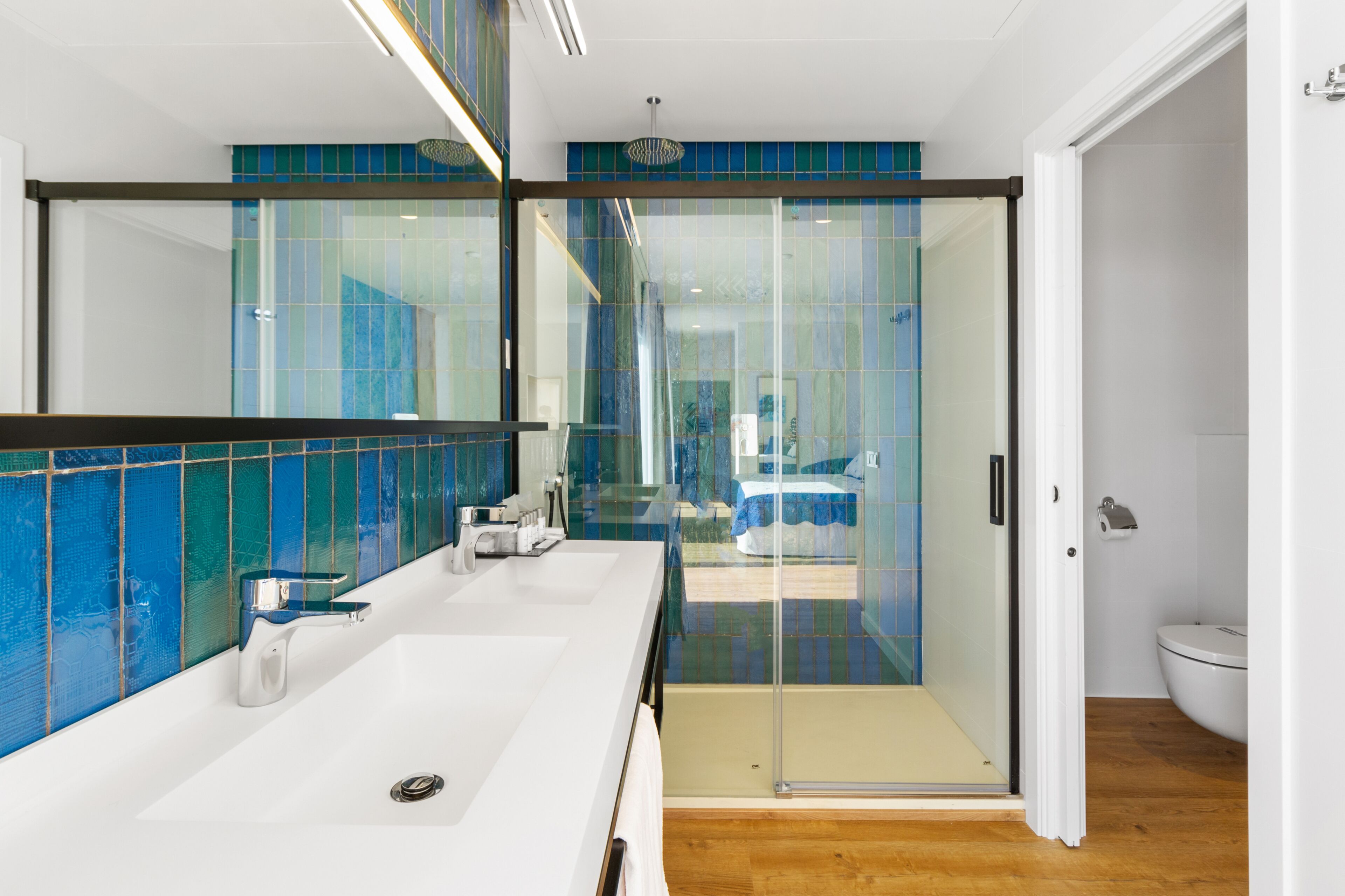 Un baño moderno con un espejo grande, dos lavamanos y una cabina de ducha de vidrio.