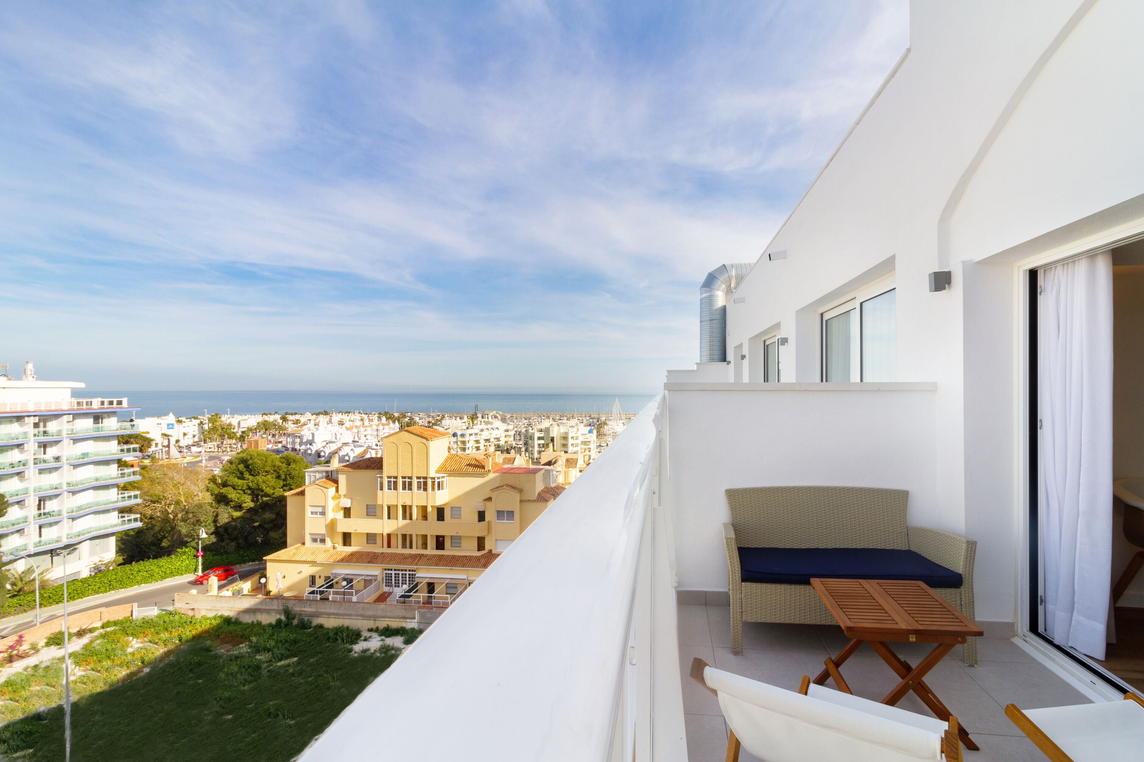 A balcony with a view of the city and sea, a wicker sofa, and a small table.