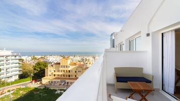 A balcony with a view of the city and sea, a wicker sofa, and a small table.