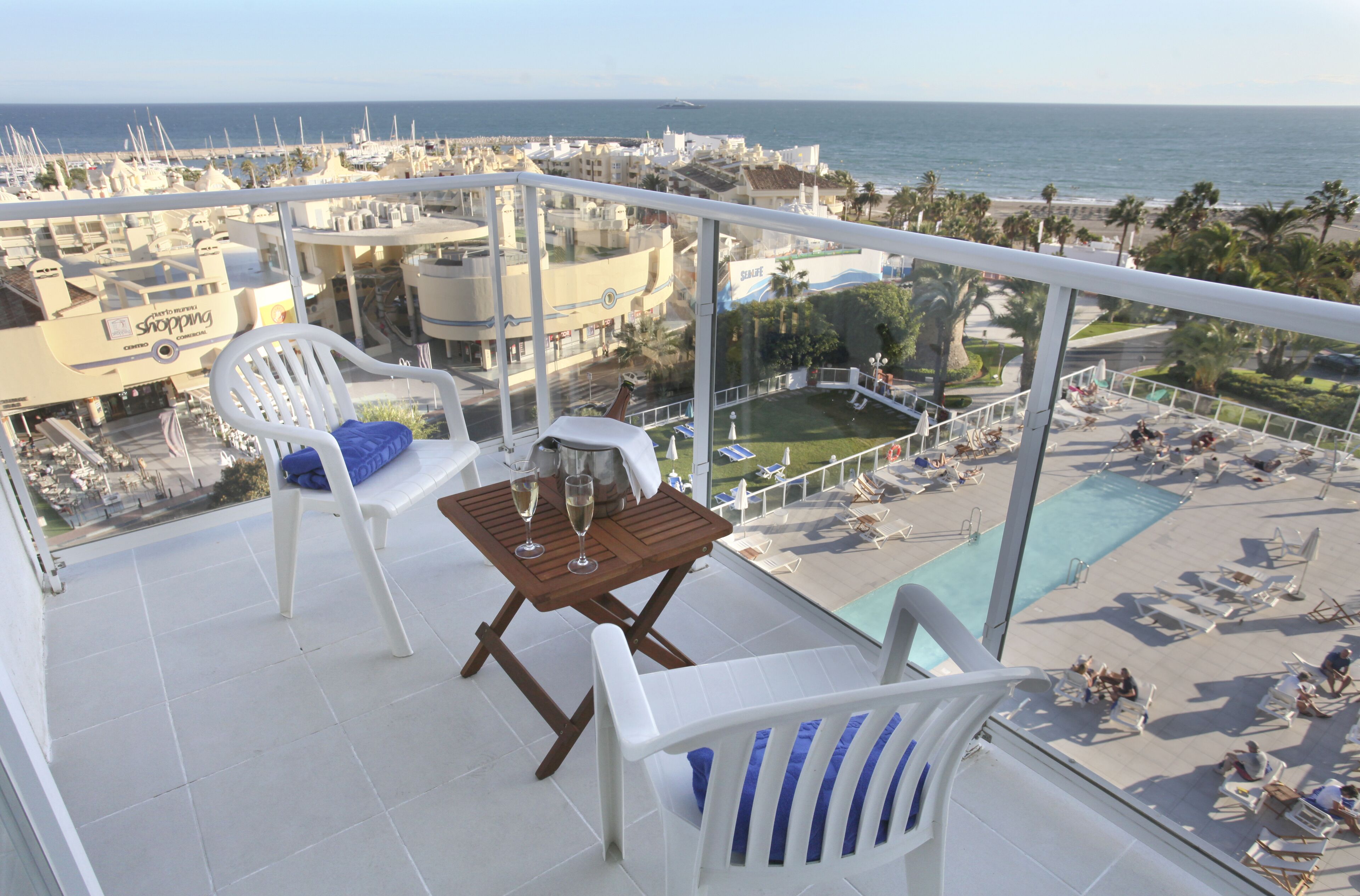 A balcony with a table, chairs, and a pool area with lounge chairs.