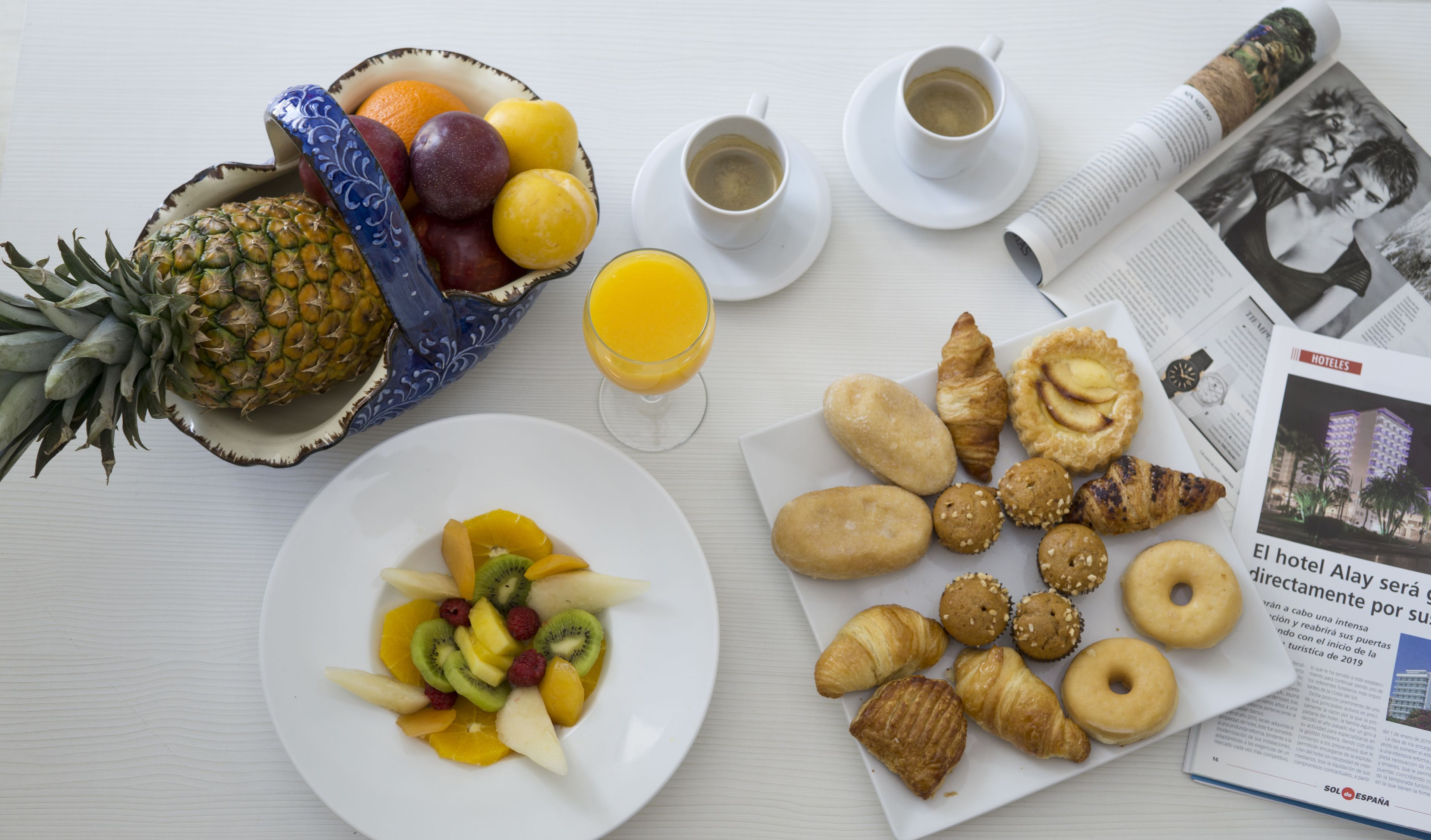 A breakfast table with fruits, pastries, coffee, and a newspaper.