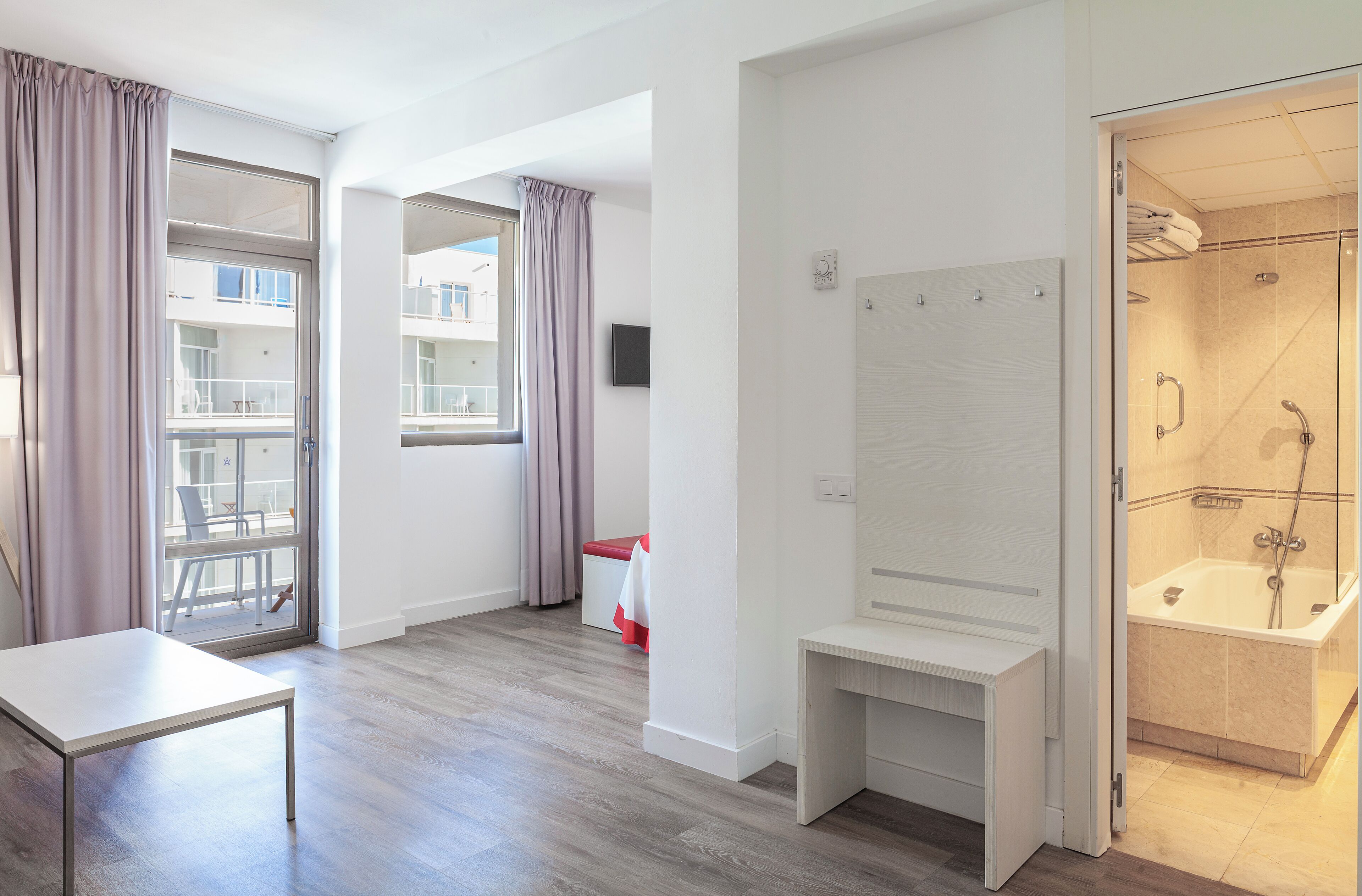 Una habitación de hotel moderna con un amplio ventanal, zona de ducha y una pequeña mesa.