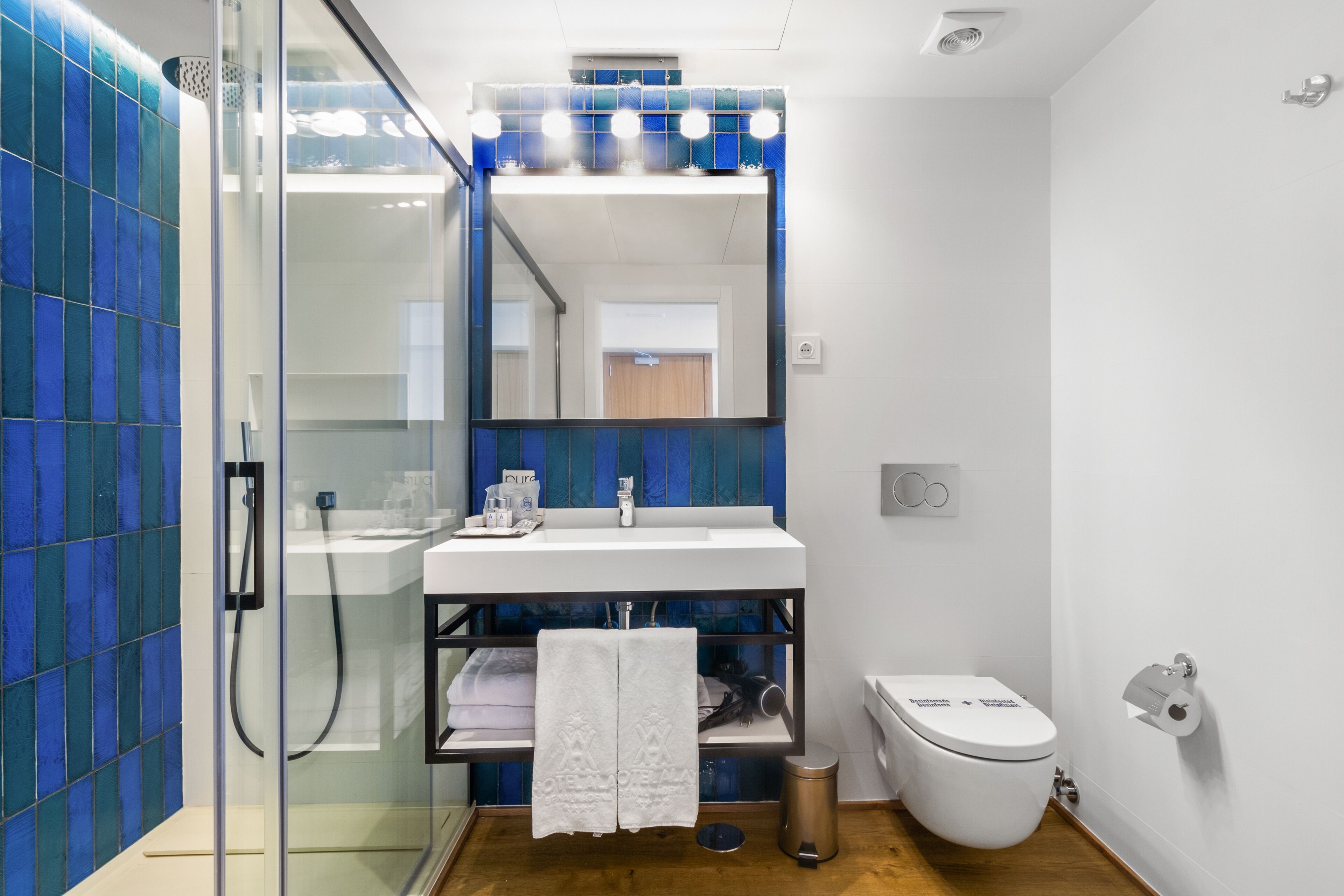 A modern bathroom with a glass shower enclosure, a white sink with a mirror above, and a toilet.