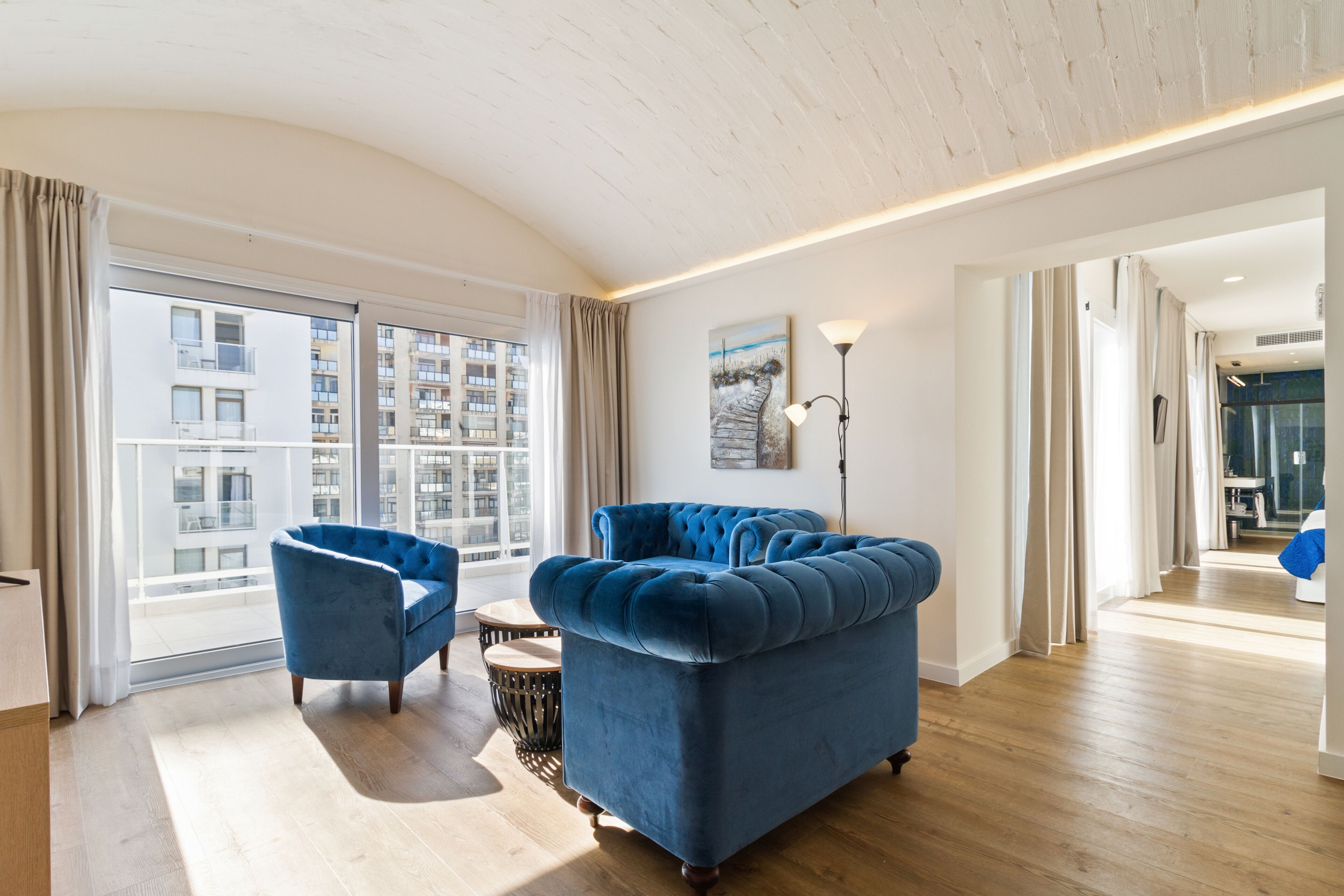 Ein modernes Wohnzimmer mit einem großen Fenster, einem blauen Sofa und einem kleinen runden Tisch.