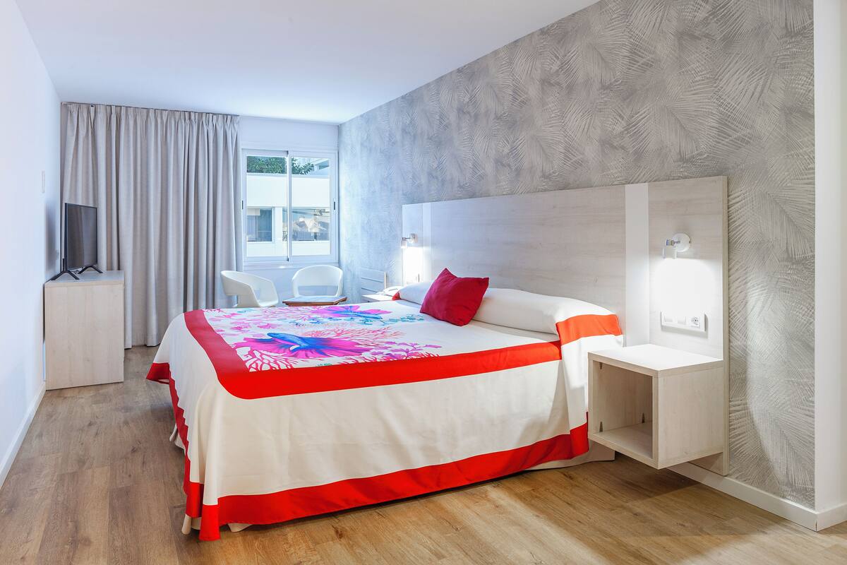 A hotel room with a bed, a desk, a chair, a TV, and a window with curtains.