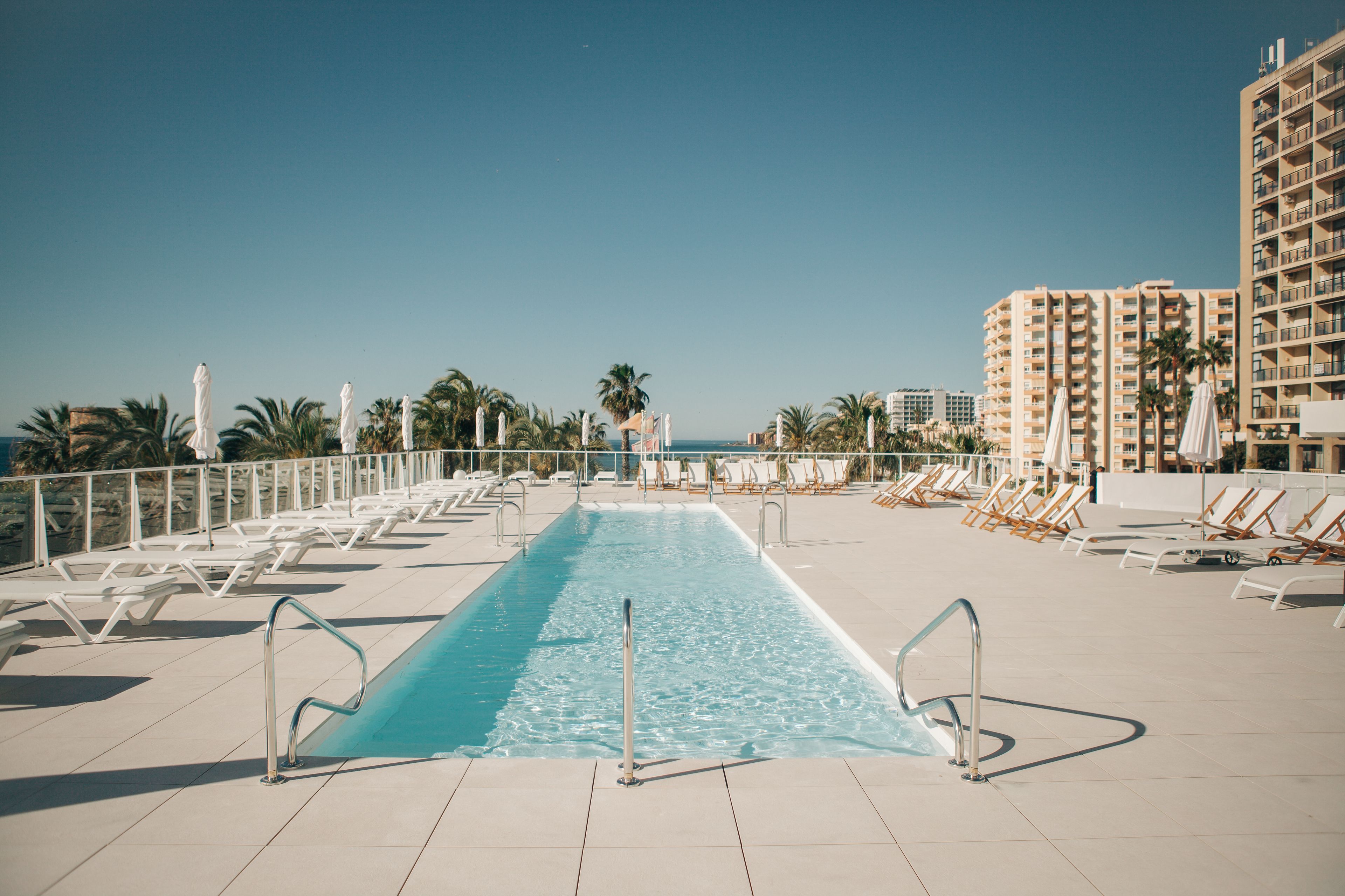 Ein Pool auf dem Dach mit Liegestühlen, Palmen und Blick auf den Ozean.