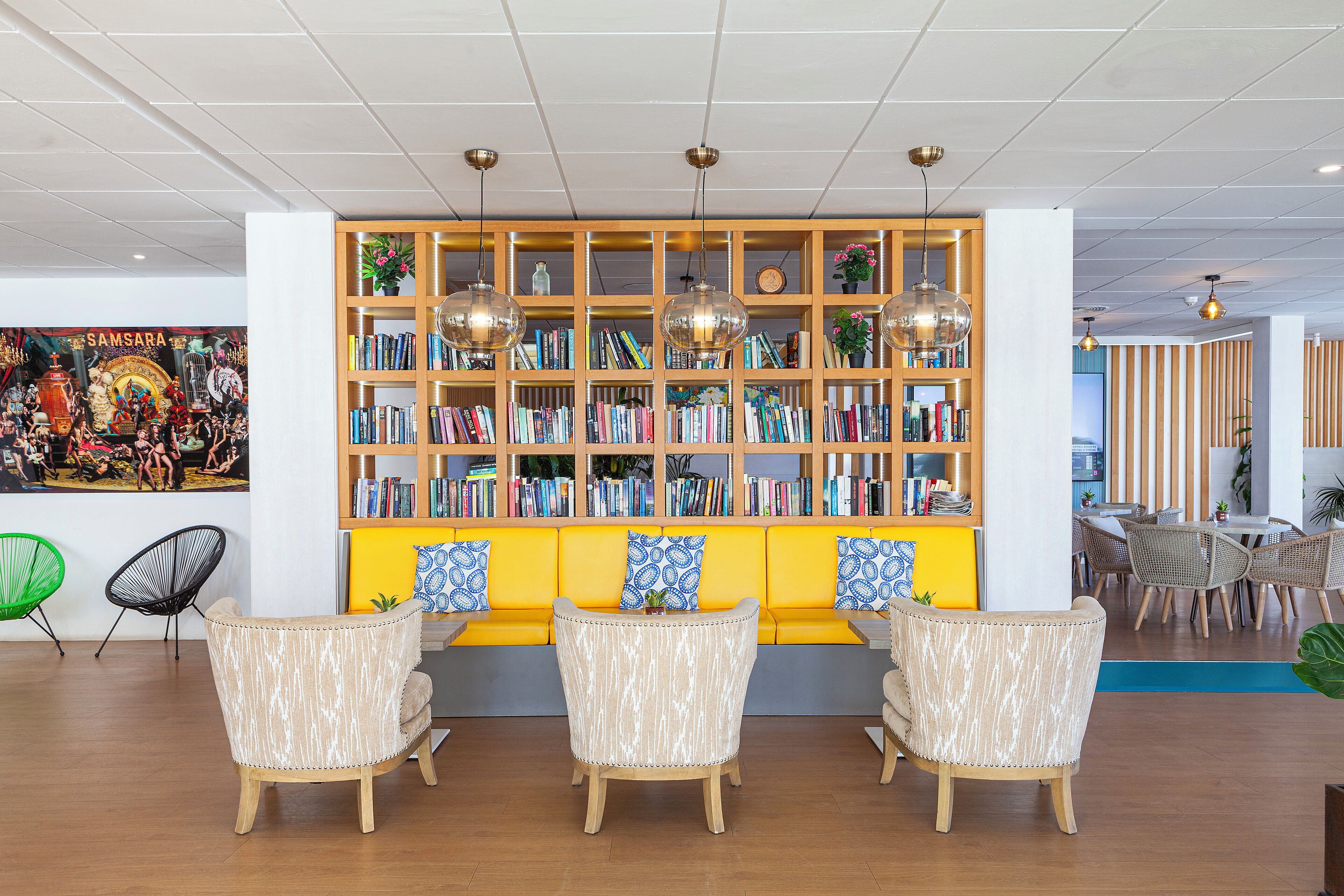 Une bibliothèque moderne avec des étagères, un canapé jaune et des fauteuils en osier.