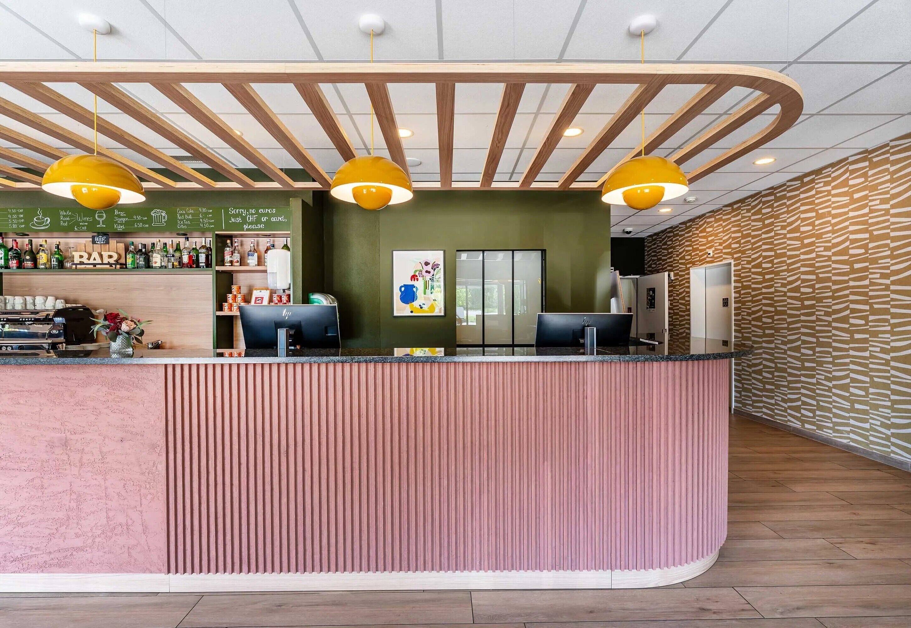 A reception area with a wooden ceiling, a pink counter, and yellow pendant lights.
