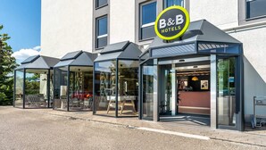 A B&B hotel with a modern glass facade, outdoor seating, and a clear view of the interior. - B&B Hotel Rothrist Olten (Rothrist)