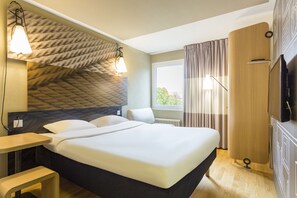A hotel room with a large bed, a desk, a wardrobe, and a television.