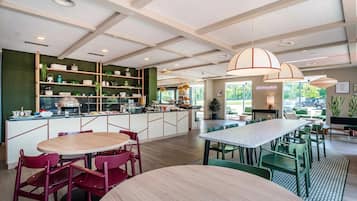 Un restaurant moderne doté d’un îlot central, de chaises vertes et de luminaires suspendus.