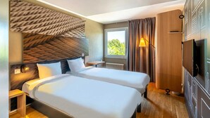 A hotel room with two beds, a small table, a TV, and a window with curtains. - B&B Hotel Rothrist Olten (Rothrist)