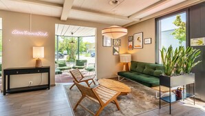 A modern living room with a sofa, chairs, a coffee table, a console table with a lamp, and a neon sign. There are framed pictures on the wall and a potted plant on a stand. - B&B Hotel Rothrist Olten (Rothrist)