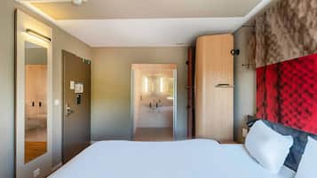 Ein modernes Hotelzimmer mit einem großen Bett, einem hölzernen Kopfteil, einem Spiegel und Blick ins Bad.